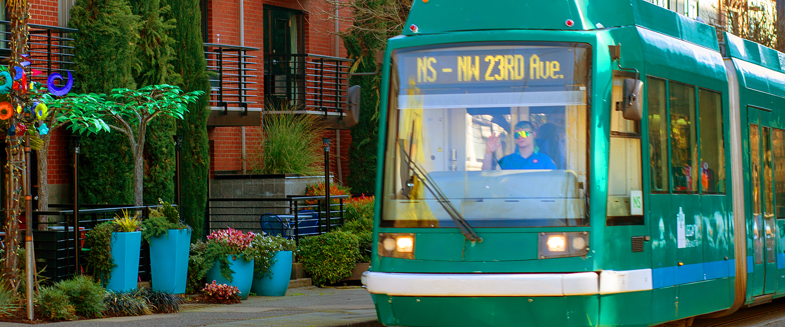 a green tram in front of a building with plants