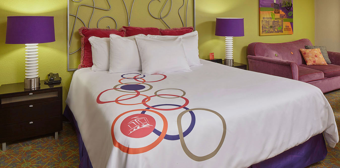 A hotel room with a large bed, two nightstands, a sofa, and colorful decor.